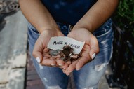 Photo of a woman's hands cupping a handful of coins with a note that reads "make a change". 