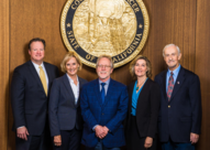 The five Placer County Board of Supervisors members in formal attire pictured before a gold county seal