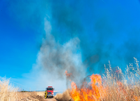 Fire Truck driving up to a wildfire in a field 