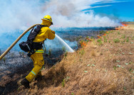 A firefighter sprays water on a grassland fire