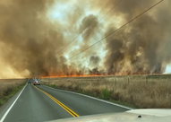 Picture of roads surrounded by dry grass on fire with big clouds of smoke in the air