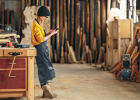 young woman working in woodshop looks at her phone