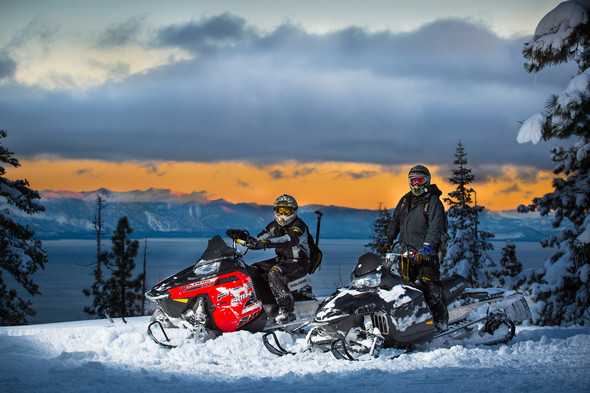 two snowmobiliers overlooking lake tahoe at sunset