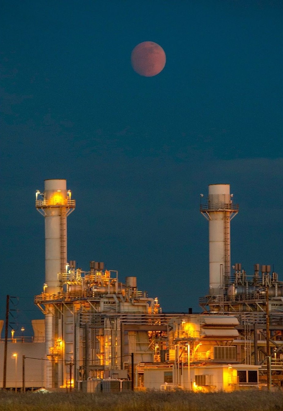 A blood moon hangs over an industrial complex in the night sky