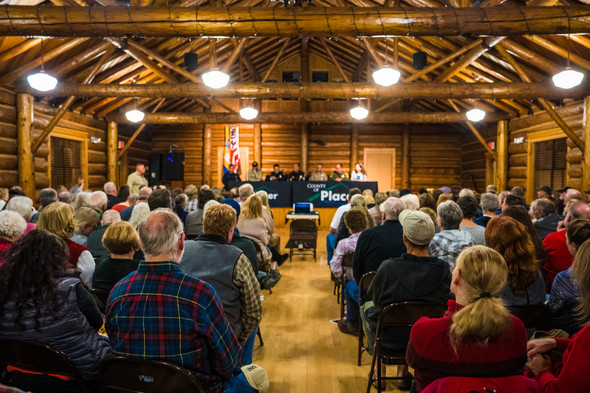 People seated at a town hall meeting in a log-paneled community meeting hall