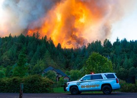 Wildfire raging behind range of pine trees - Placer County Sheriff's Office SUV parked in front of threatened house