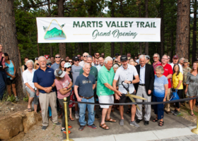 martis valley trail grand opening banner over a crowd of people standing on trail head with giant pair of scissor cutting a ribbon