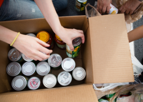 person putting canned goods in a cardboard box