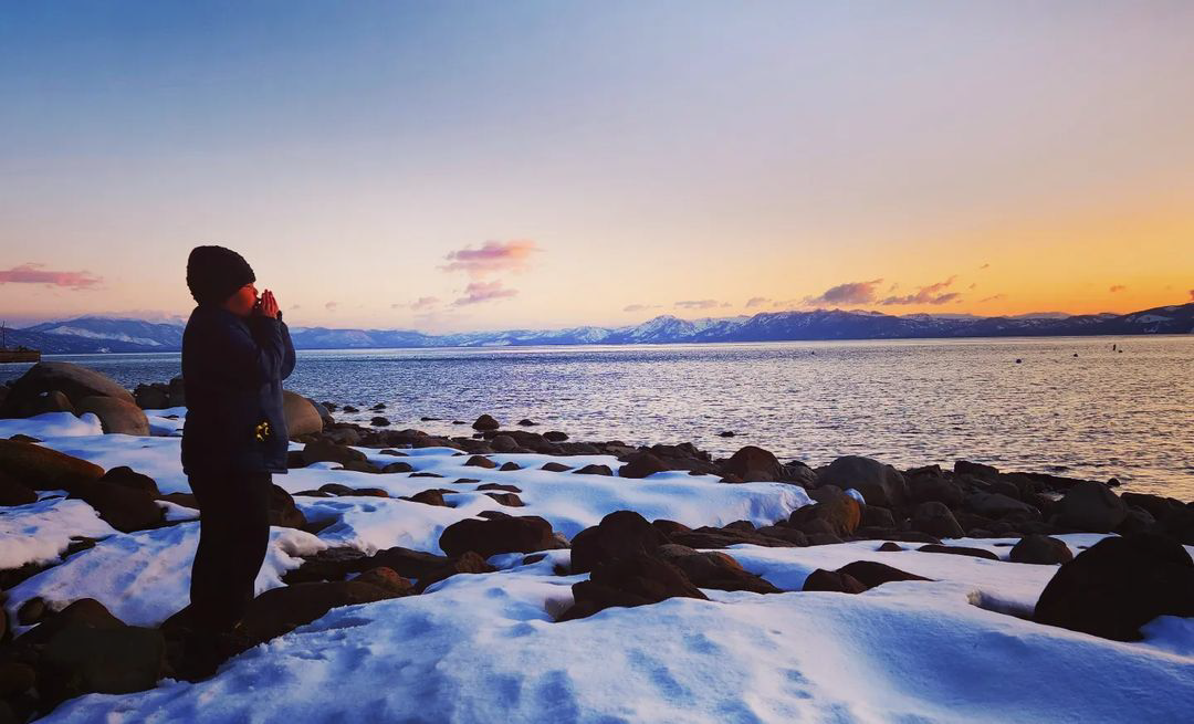 young boy standing along snow covered shore in Lake Tahoe