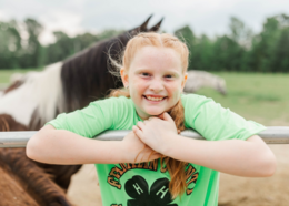 Placer County girl in green 4-H shirt smiles in front of horses