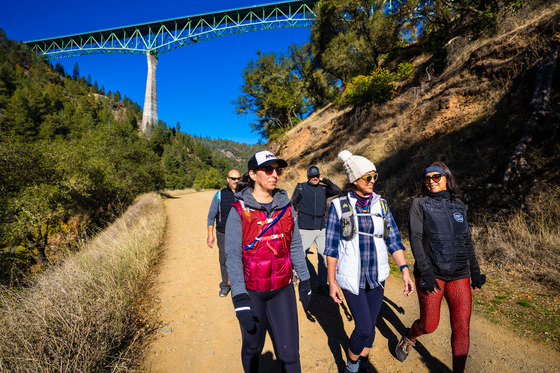 Members of the Latino Leadership Counsel hike a trail in front of the Foresthill bridge