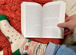Person with cozy socks and a knitted blanket reads a book