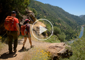 Image of two hikers on open trail leading to river 