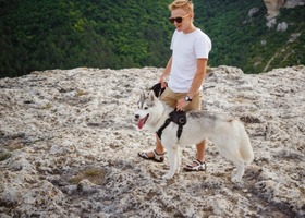 Man on hike on cliff with pet dog on leash