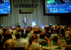 A speaker is shown on-stage at the Placer Valley 2023 event in front of a crowd.