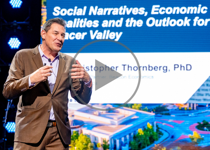 A play button icon is on top of a photo of Dr. Christopher Thornberg of Beacon Economics addressing the crowd during a speech at Placer Valley 2024.