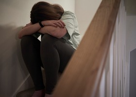 A woman seated on a staircase burying her face in her arms 