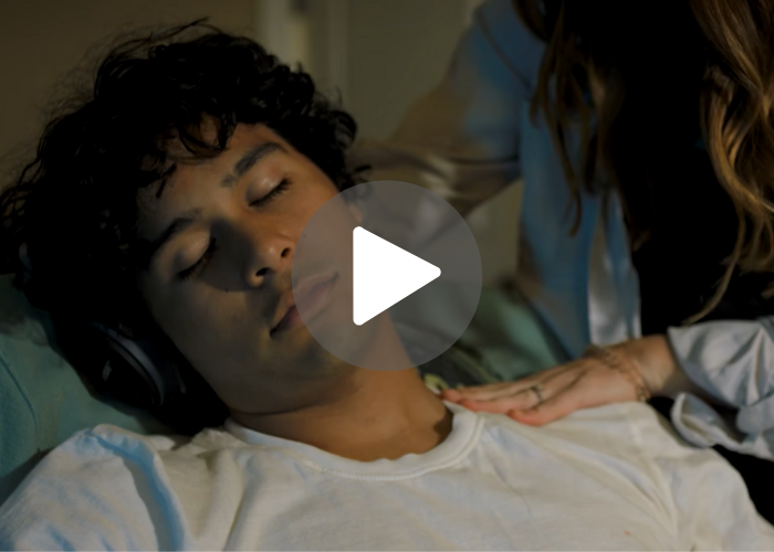 A woman tries to shake awake a young man who appears to be sleeping