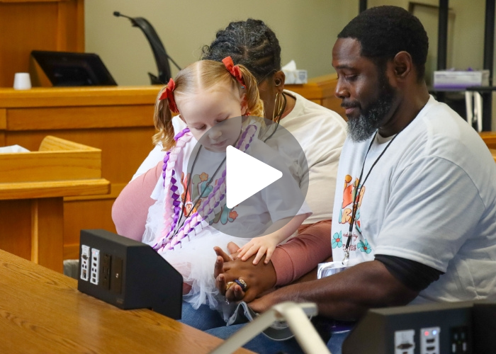Young girl takes the hand of adoptive father at adoption ceremony.