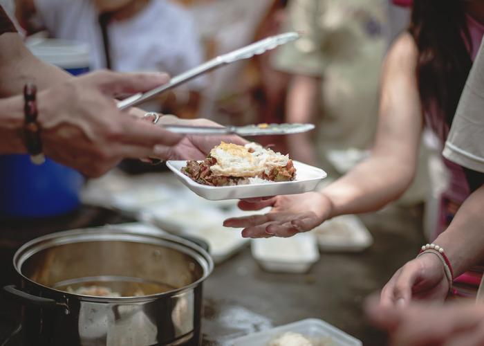 A server hands a plate of food to a recipient in a serving line.