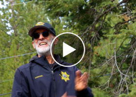 Animal control officer standing in front of pine trees in Tahoe, with video play overlay