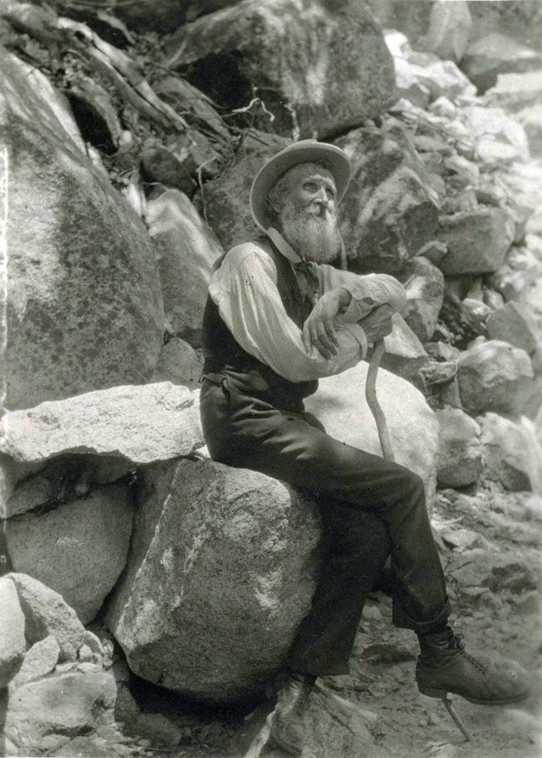 Black and white photo of a man perched on a boulder looking skyward