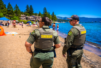 Two green uniformed Placer County Sheriff's Office deputies on a beach in Tahoe.