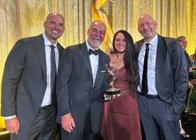 Four people in formal attire pose with an golden statuette at an award ceremony