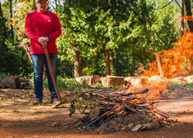 A man with a rake observes a pile of burning branches