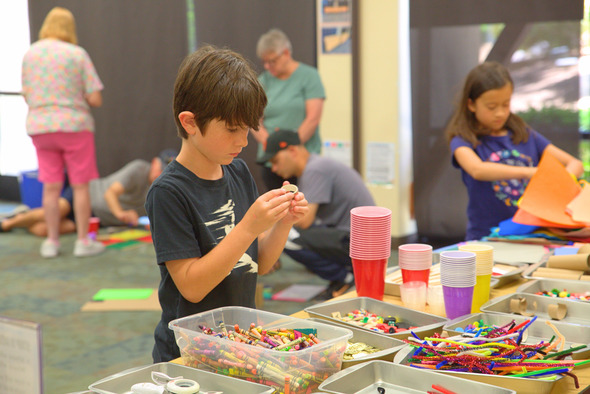 Photo of boy looking at craft tape over table of crayons, tape, scissors and more supplies.