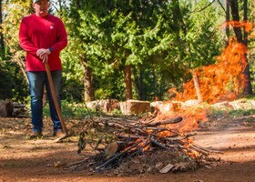 A man holding a pickaxe monitors a brush pile fire in a forest clearing