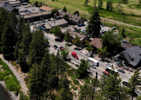 Aerial of the Tahoe City town center with cars on state Route 28 surrounded by large green trees on a sunny day.