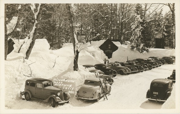 1930’s era photo of a row of cars parked along a tall snow embankment
