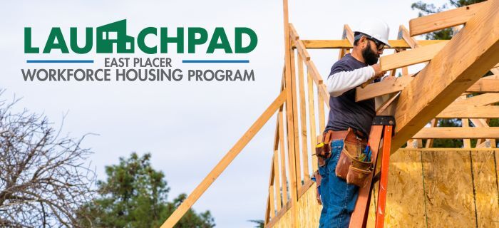 A home being built with a wood frame on a blue-sky day and the county's Launchpad program badge.