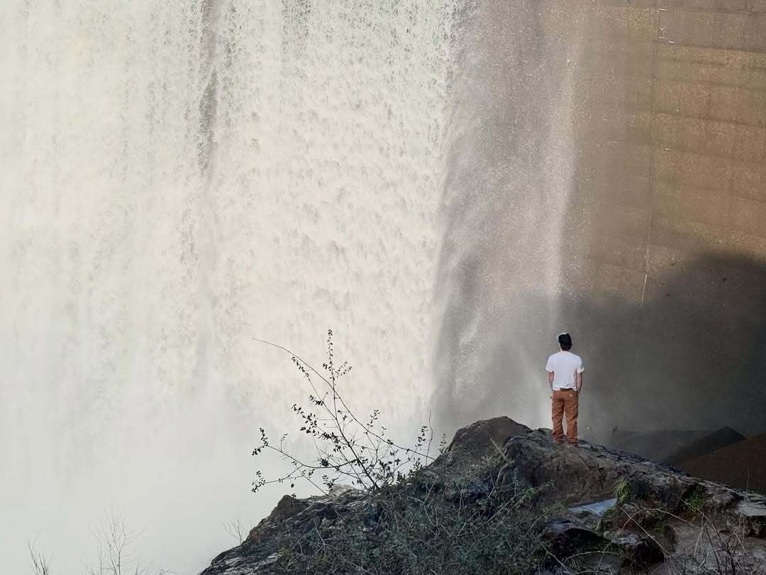 man stands in front of water spilling over dam