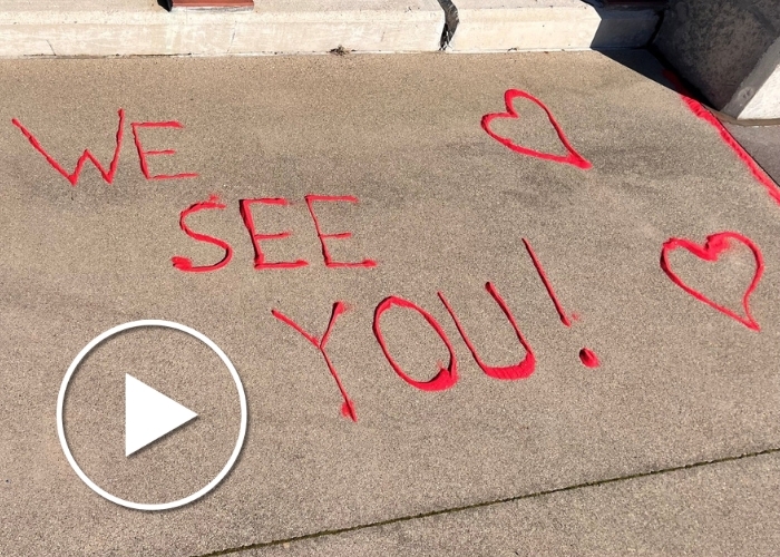 Red sand spelling 'We see you!' on the concrete from a recent PCOE event with a play button.