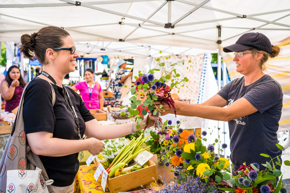 Two women handling a transaction at a farmer's market, both holding a bouquet of flowers being exchanged
