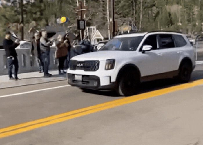 GIF of 2 cars driving over a bridge with a crowd of people on the sidewalk