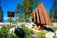 Picture shows a metal art exhibit in the middle of a roundabout groomed with flowers and showing Lake Tahoe in the background