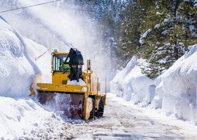 A yellow snow blower blasts snow to the side of a snow-covered street