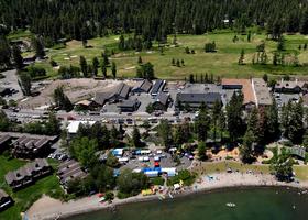 An aerial image of Tahoe City on a sunny day with green trees and a busy North Lake Tahoe Boulevard featured.