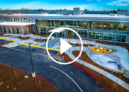 The HHS Conference Center exterior, a glass building with a play button overlayed with sun and clouds in the background
