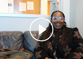 Social worker smiling and sitting in a loveseat with a play button overlay.
