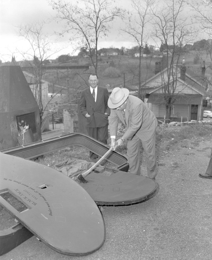 A man wearing a suit and a wide-brimmed hat uses an axe to destroy a gambling table
