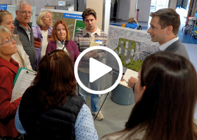A group of people inside a high school cafeteria in a huddle talking to a man in a suit
