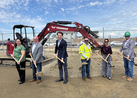 Six people holding shovels in front of construction equipment