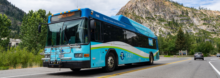 A blue TART bus on the roadway in front of mountains in Olympic Valley.
