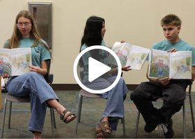 Three teenagers in chairs in teal t-shirts and jeans showcasing the new book and reading it.
