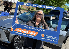 A woman poses with a photo frame in front of an electric car
