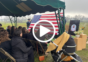 Photograph of a funeral service featuring the family of the soldier who lost his life and a United States flag.